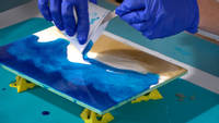 Christine pouring blue resin onto board to create the ocean Thumbnail